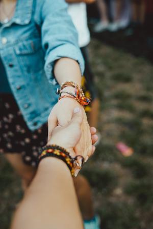 Person holding the hand of a woman. Each have bracelets around their wrists.