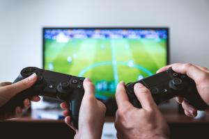 Two pairs of hands holding Playstation controllers playing a soccer video game