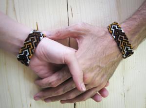 two people holding hands wearing matching friendship bracelets colors brown, white, black, gold. 