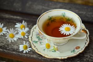 Tea cup with tea inside. Daisies are sprinkled around the cup. 