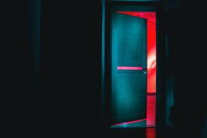 Dark room with white door that opens to another room lit with red light.